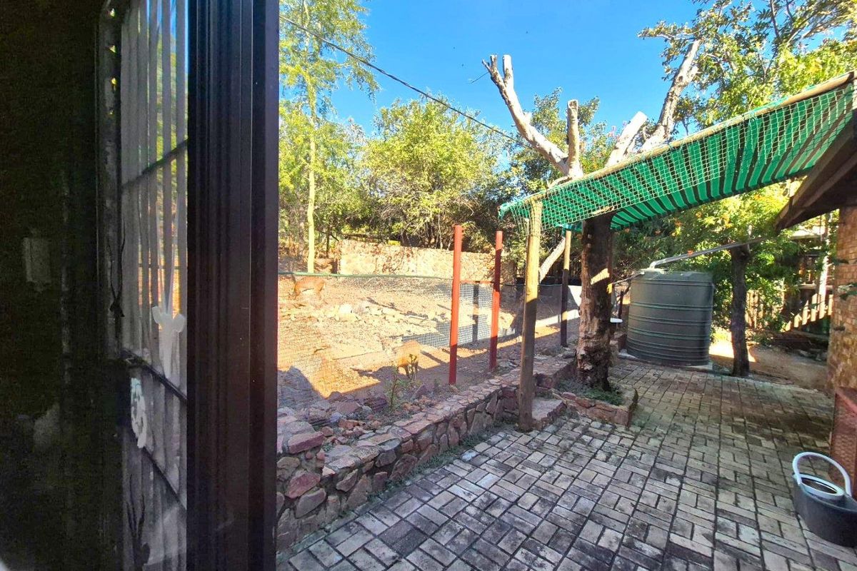 A rear outdoor area featuring paved flooring, a water storage tank, and a shaded structure, set within a natural garden environment.