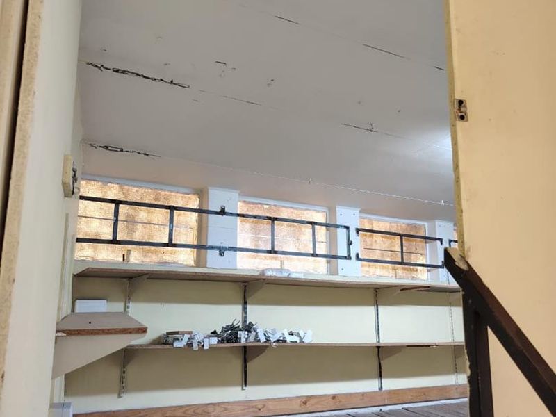 A vacant utility or storage space featuring timber flooring, wall-mounted shelving, and security bars on the windows, requiring significant refurbishment.