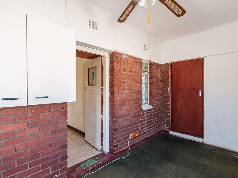 An empty utility or transition space featuring exposed brick walls, tiled flooring, and a ceiling fan, offering potential for renovation or functional storage.