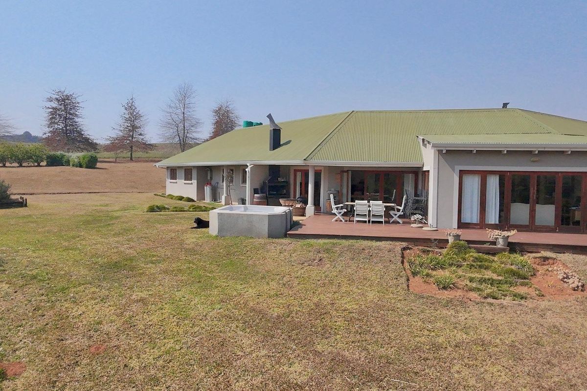 Rear view of the farmhouse featuring a covered patio, built-in braai area, and a raised spa pool set within a spacious garden landscape.