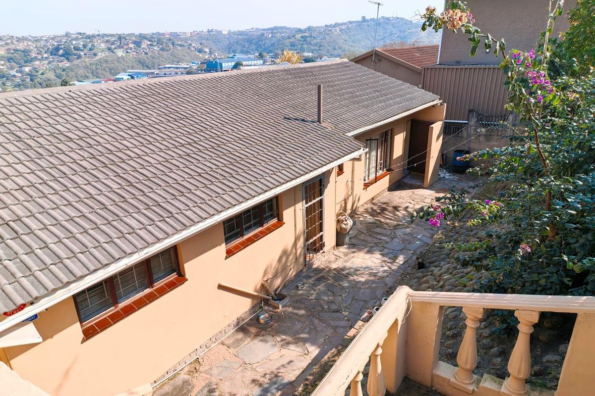 Rear exterior view of the property featuring a stone-paved patio area, concrete tiled roof, and a balustrade overlooking the surrounding landscape.