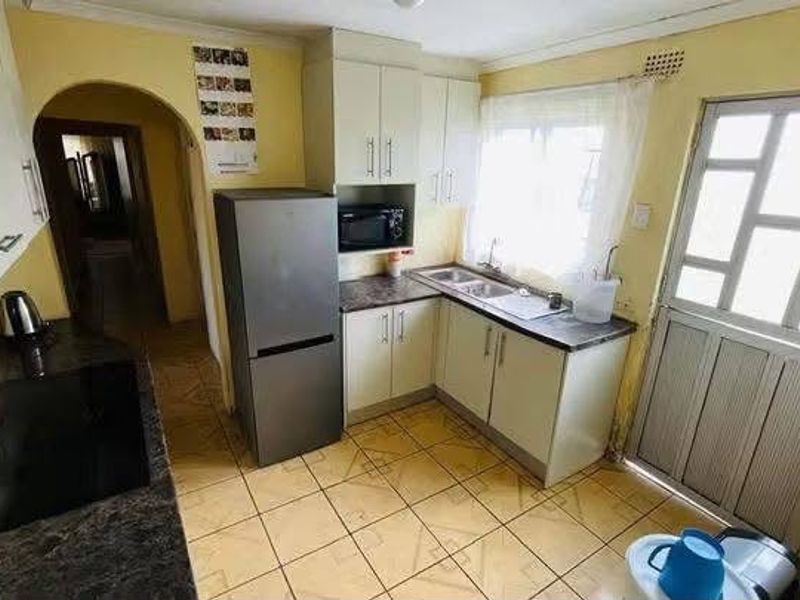 A functional kitchen featuring built-in cabinetry, laminate countertops, a double sink, and tiled flooring, providing a practical workspace with direct exterior access.