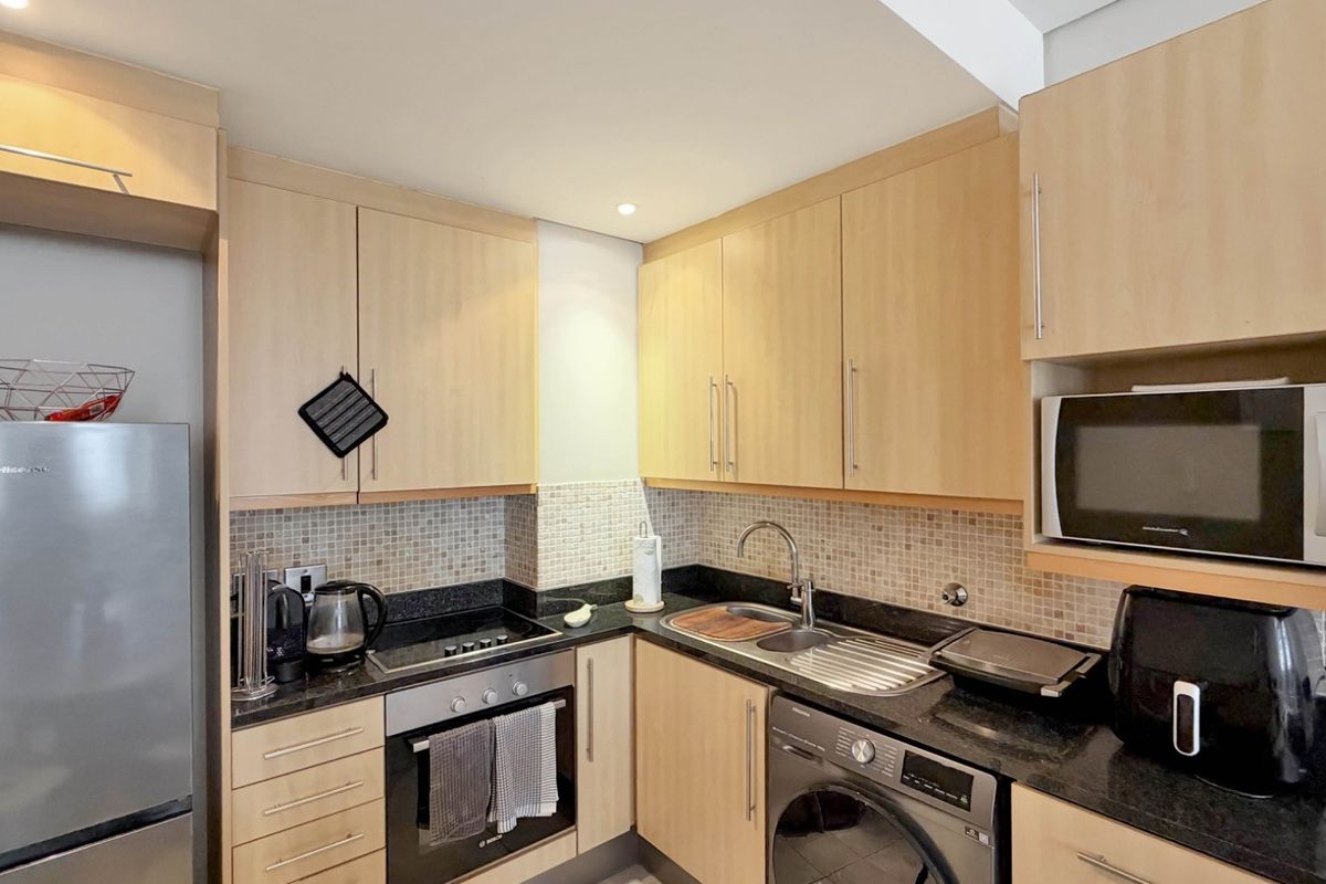 Compact kitchen featuring light wood cabinetry, granite countertops, mosaic tile backsplash, and integrated appliances including an oven, hob, and washing machine.