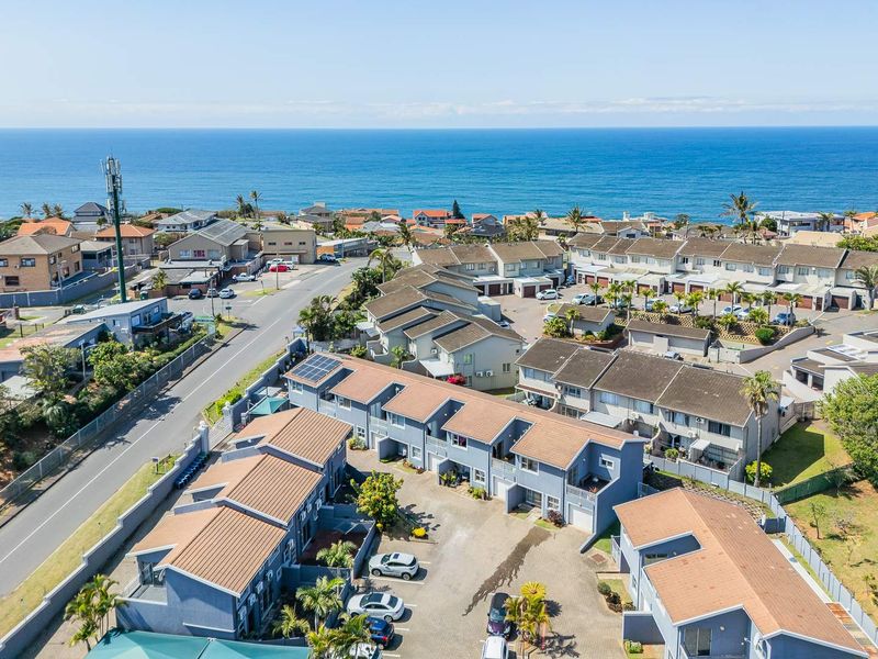 Aerial view of a coastal residential apartment complex featuring tiled roofs, solar panels, and paved driveway access near the ocean.