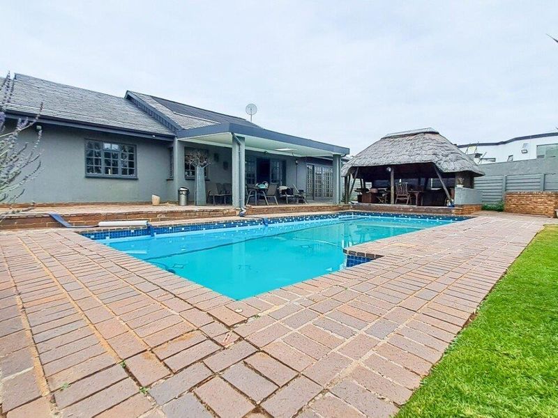 Outdoor pool area featuring a swimming pool, brick paved surround, covered patio, and a traditional thatched lapa for outdoor entertainment.
