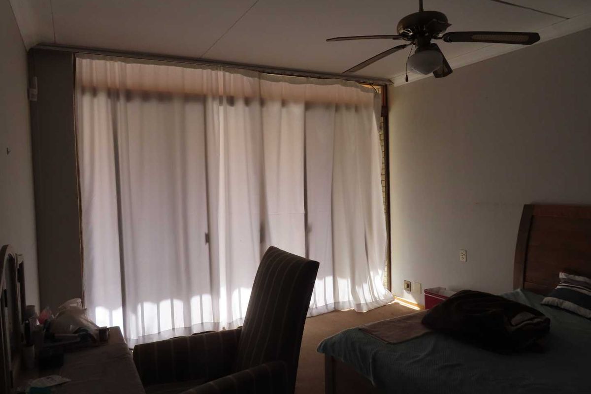 A bedroom featuring a ceiling fan and large sliding glass doors with curtains, providing natural light and access to the exterior.