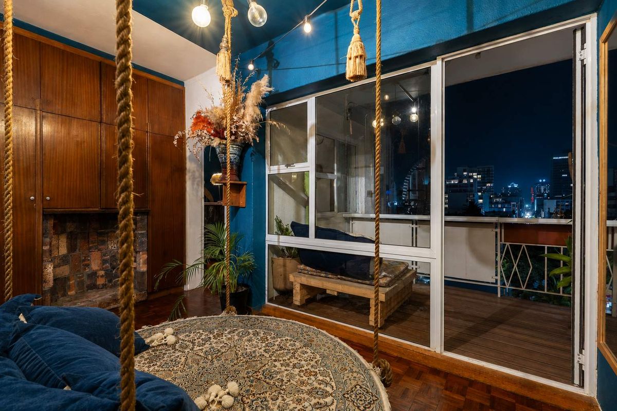A cozy living room featuring rich parquet flooring, built-in wooden cabinetry, an exposed brick fireplace, and direct access to a private balcony with city views.