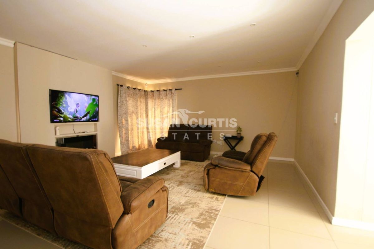 A spacious living room featuring neutral tiled flooring, recessed downlighting, and coving, providing a comfortable and functional area for relaxation.