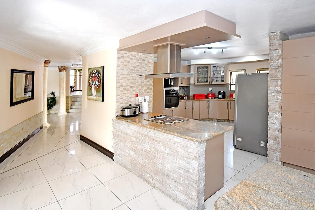 Modern kitchen featuring granite countertops, built-in oven, electric hob, and stone-clad breakfast bar, seamlessly integrated into an open-plan living space with tiled flooring.