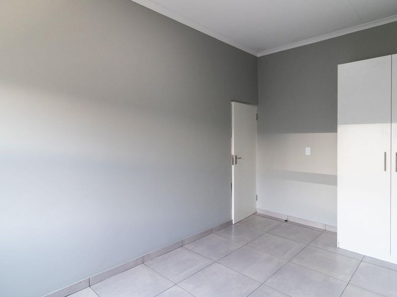 A clean, empty bedroom featuring neutral grey walls, tiled flooring, and a built-in white wardrobe.