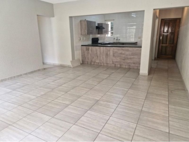 An open-plan living area featuring tiled flooring and a functional kitchen with built-in cabinetry, a sink, and an extractor fan.