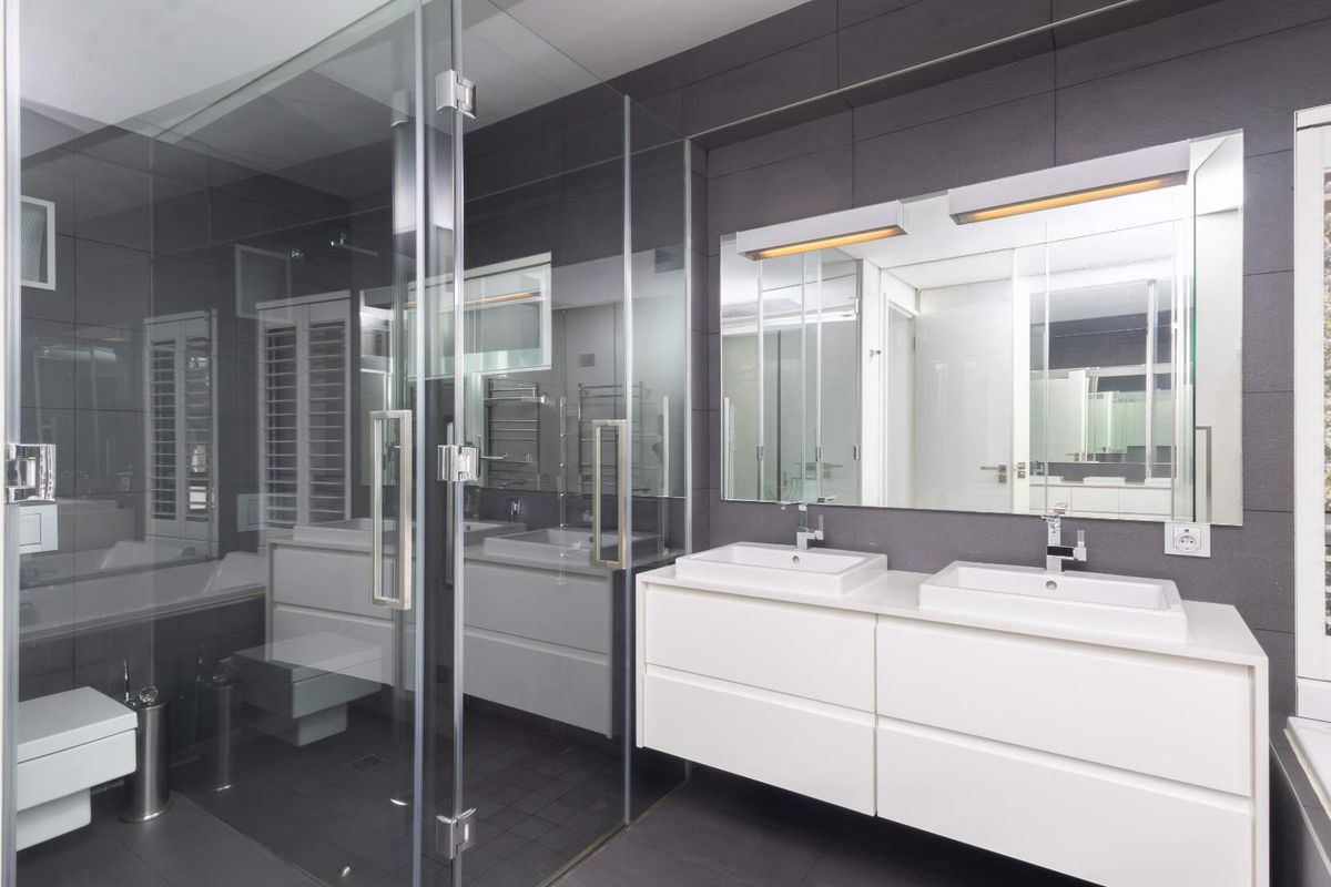 Modern bathroom featuring a double vanity with wall-mounted cabinetry, a glass-enclosed shower, wall-hung toilet, and contemporary dark tile finishes.
