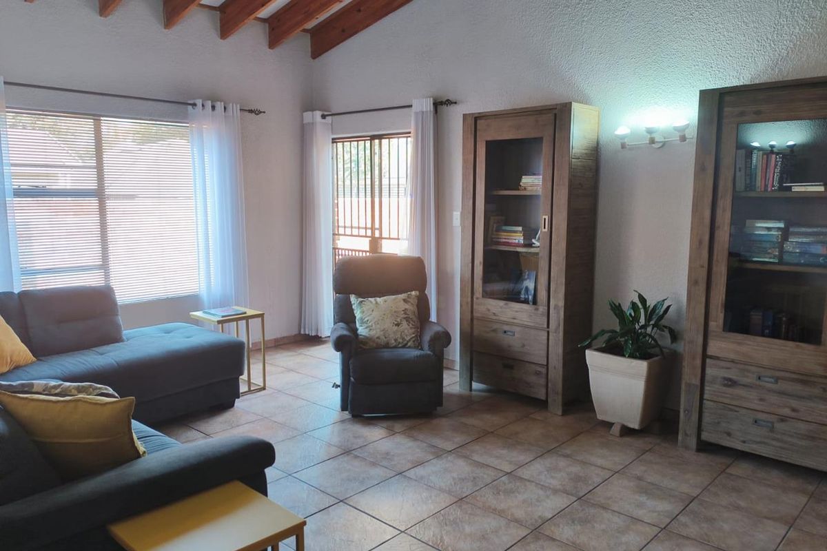 A living room featuring exposed timber ceiling beams, ceramic tiled flooring, and a sliding glass door with security gate leading to the exterior.