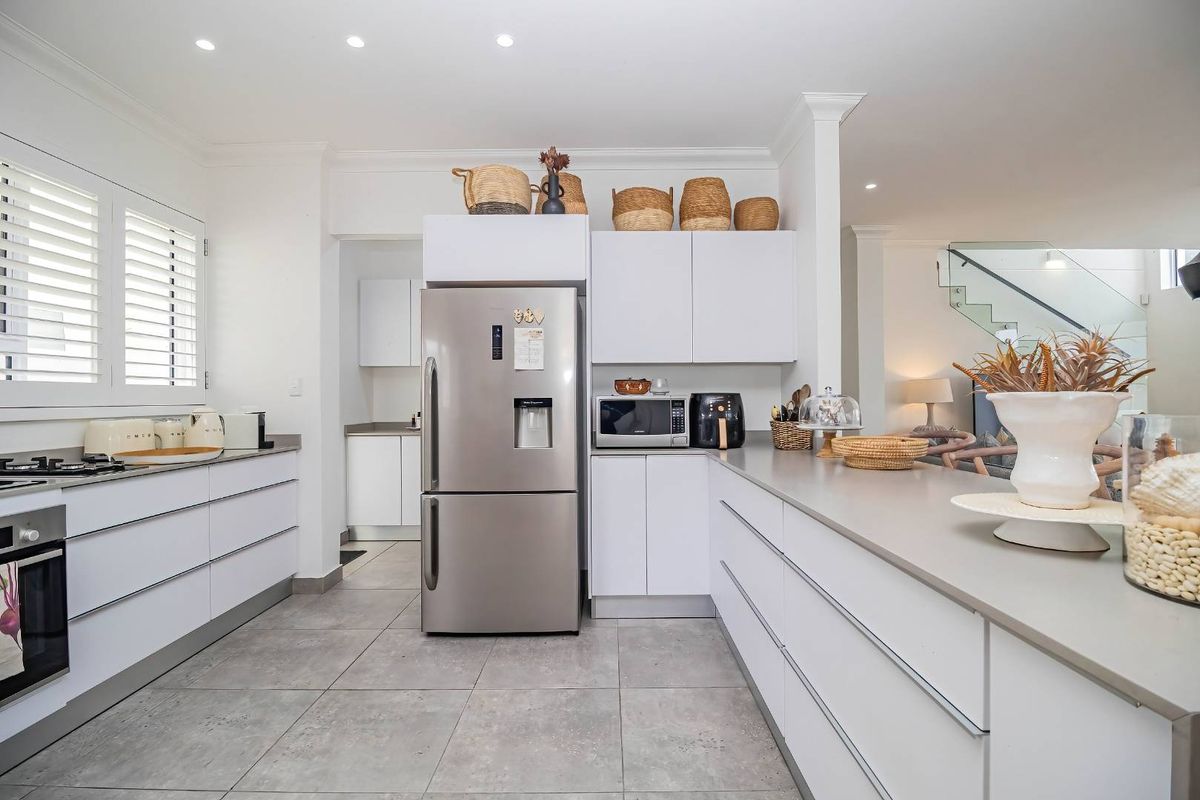 Modern kitchen featuring sleek white cabinetry, stone countertops, integrated appliances, gas hob, and tiled flooring, with an open-plan flow to the living area.