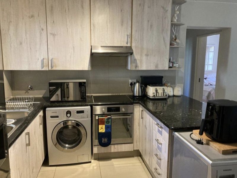 A functional kitchen featuring light wood-grain cabinetry, dark granite countertops, integrated oven and hob, and tiled flooring.