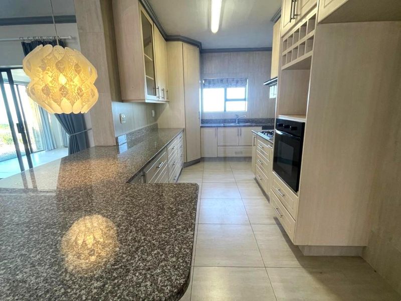 A functional kitchen featuring granite countertops, built-in cabinetry, integrated oven and hob, and tiled flooring with a breakfast bar area.