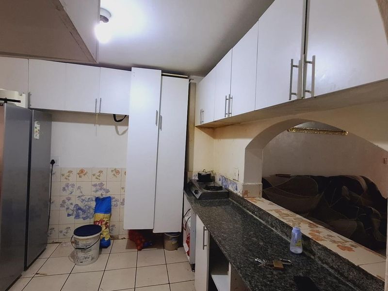A functional kitchen featuring white built-in cabinetry, granite countertops, and an open archway connecting to the adjacent living area.