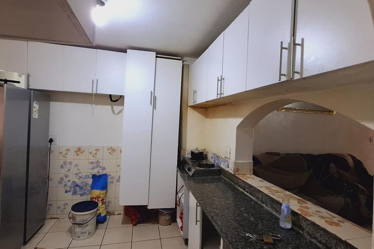 A functional kitchen featuring white built-in cabinetry, granite countertops, and an open archway connecting to the adjacent living area.