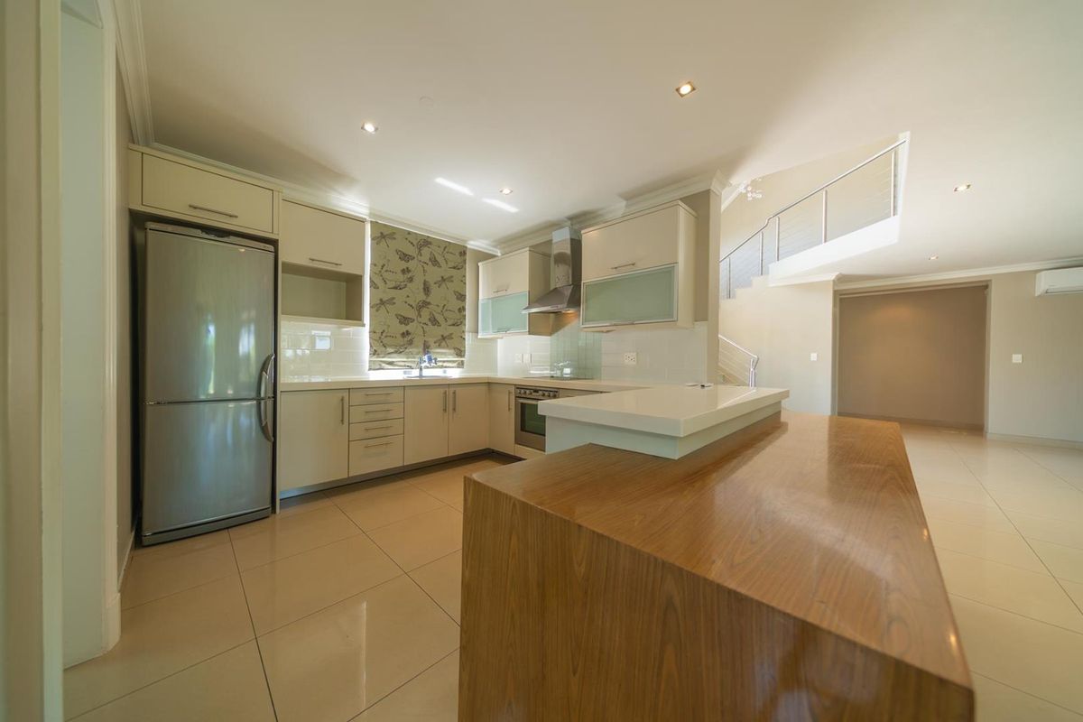 Modern kitchen featuring sleek cabinetry, stone countertops, a central island, and integrated appliances, seamlessly flowing into the open-plan living area.