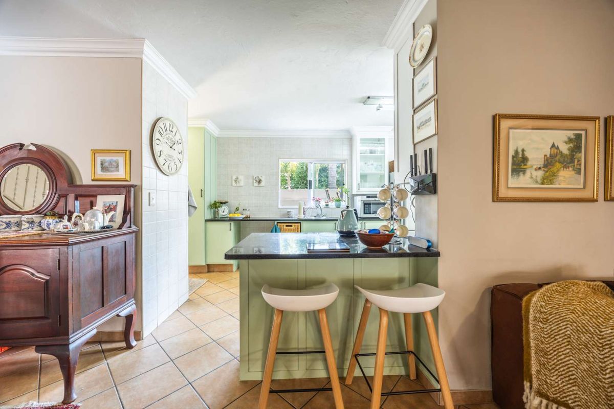A well-maintained kitchen featuring light green cabinetry, dark stone countertops, a breakfast bar, and tiled flooring, offering a functional and inviting cooking space.