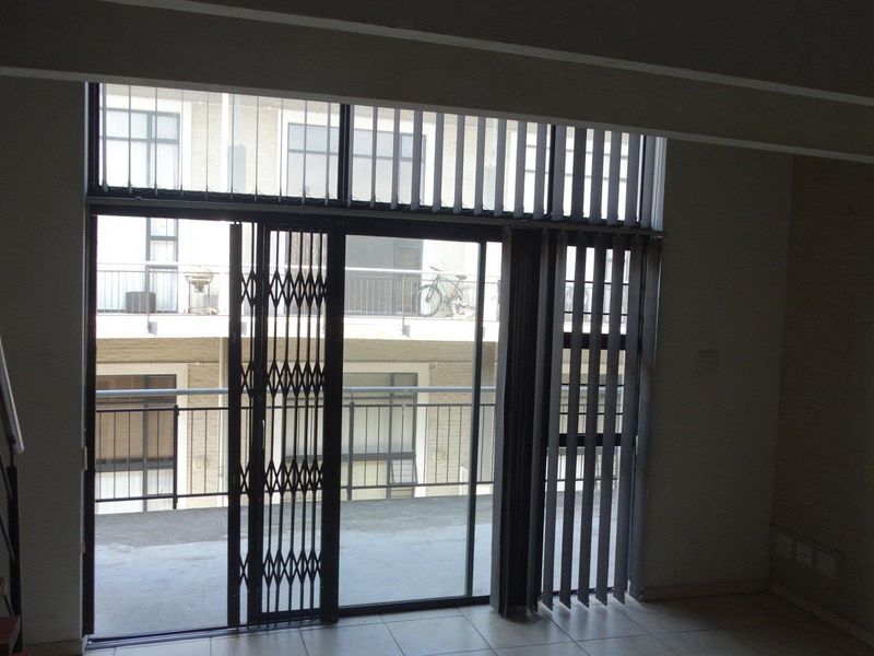 An empty living area featuring tiled flooring, a staircase, and a sliding glass door with a security gate leading to a balcony.