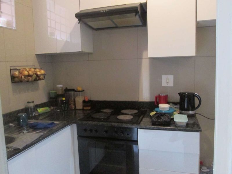 Compact kitchen featuring granite countertops, white cabinetry, built-in oven, electric hob, and an extractor fan with tiled backsplash.