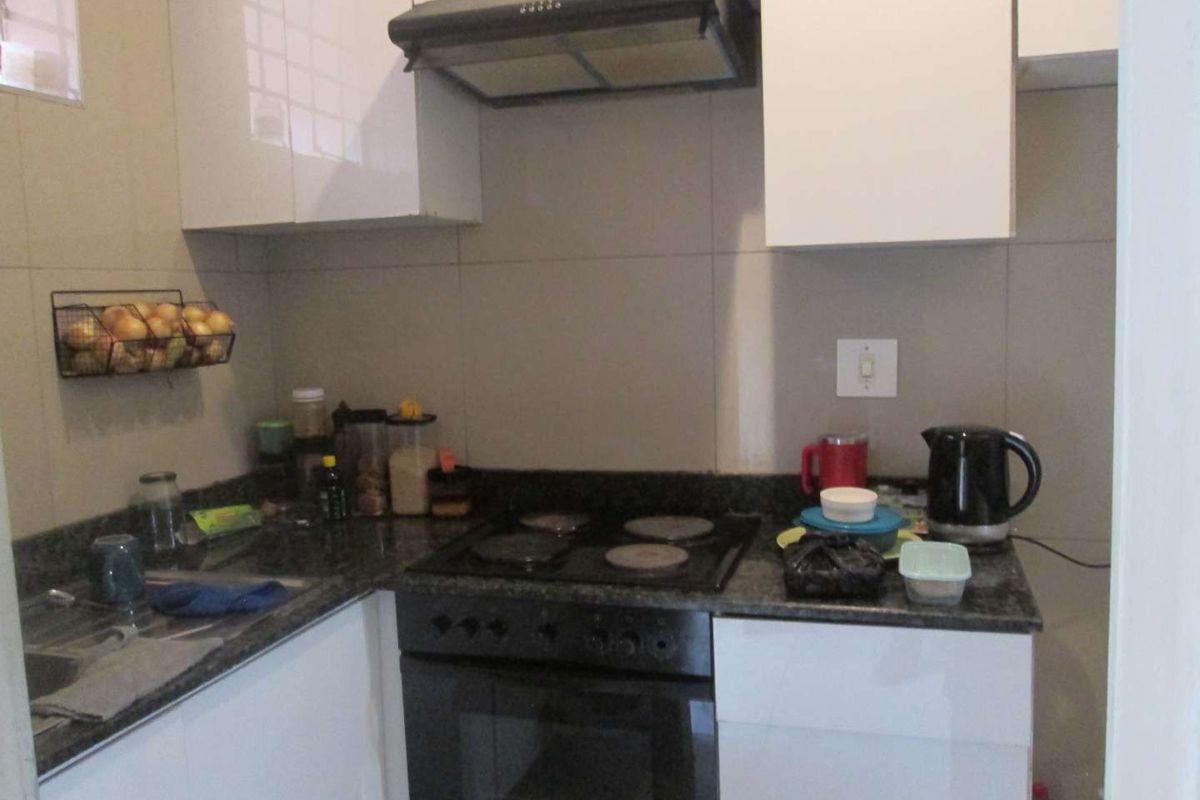 Compact kitchen featuring granite countertops, white cabinetry, built-in oven, electric hob, and an extractor fan with tiled backsplash.
