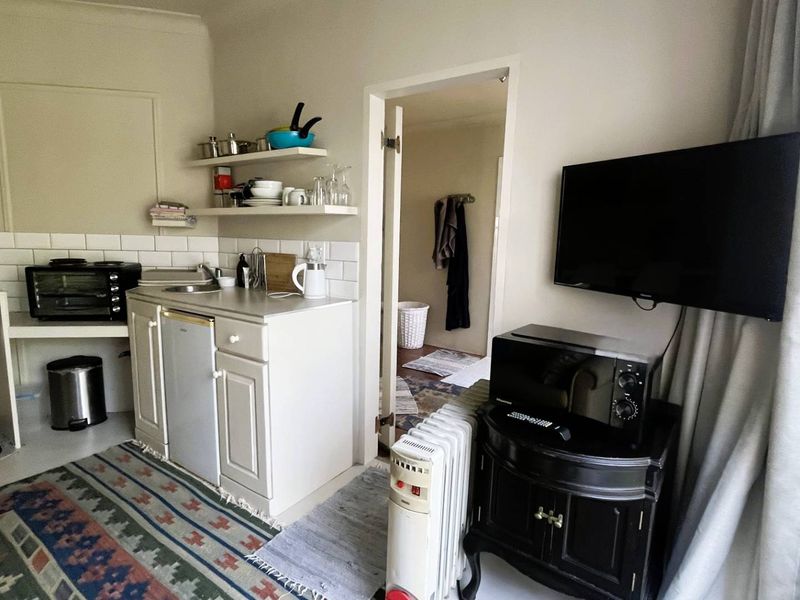 Compact kitchenette area featuring white cabinetry, subway tile backsplash, and open shelving, providing essential prep space within the cottage living area.