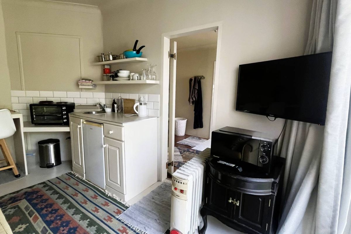 Compact kitchenette area featuring white cabinetry, subway tile backsplash, and open shelving, providing essential prep space within the cottage living area.