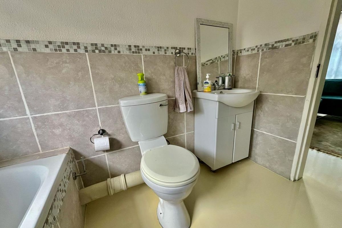 A functional bathroom featuring a standard toilet, vanity basin with storage, and tiled wall accents.