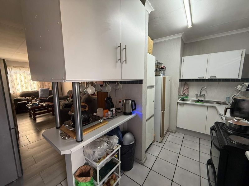 Open plan kitchen featuring white cabinetry, tiled flooring, and a breakfast counter, seamlessly connecting to the adjacent living area.