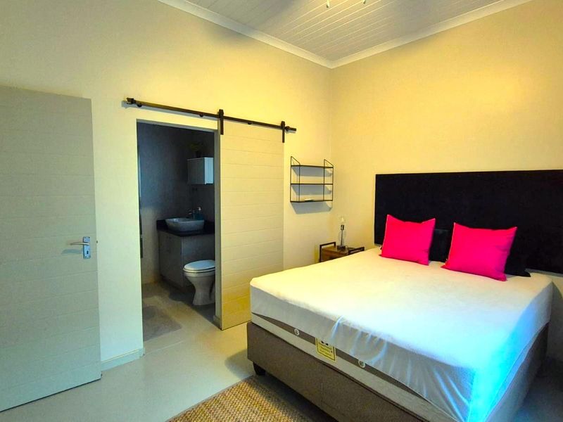 A well-maintained bedroom featuring a sliding barn door leading to an en-suite bathroom, neutral tiled flooring, and a classic tongue and groove ceiling.