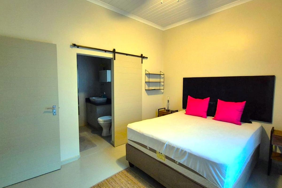 A well-maintained bedroom featuring a sliding barn door leading to an en-suite bathroom, neutral tiled flooring, and a classic tongue and groove ceiling.
