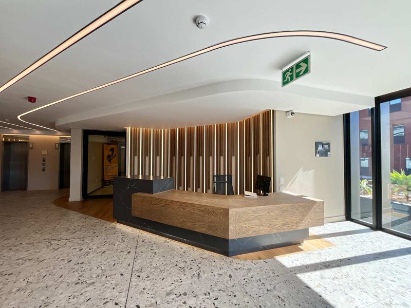Modern office lobby featuring a custom timber and stone reception desk, terrazzo flooring, and sophisticated recessed linear lighting.