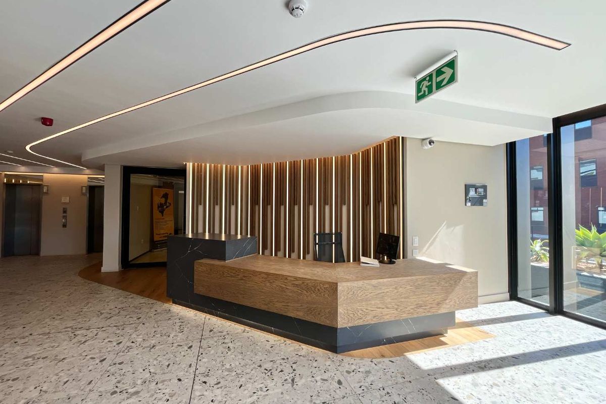 Modern office lobby featuring a custom timber and stone reception desk, terrazzo flooring, and sophisticated recessed linear lighting.
