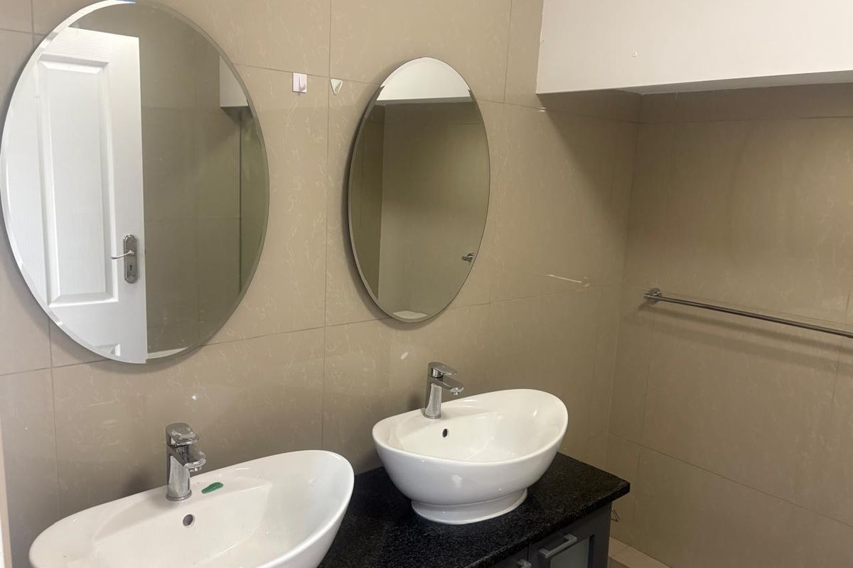 A modern bathroom vanity featuring dual vessel sinks, granite countertop, and twin oval mirrors mounted on tiled walls.