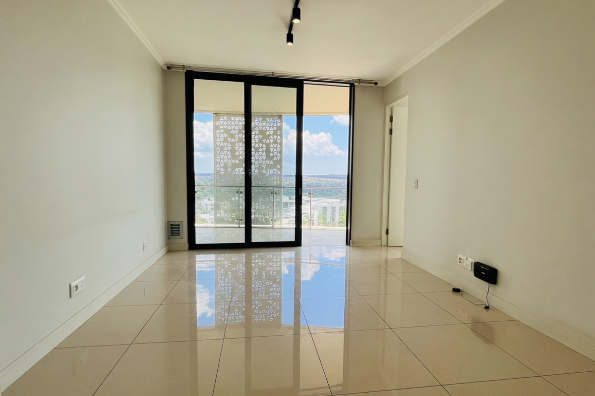A bright, empty living area featuring polished tile floors, modern track lighting, and large sliding glass doors opening to a balcony with scenic views.