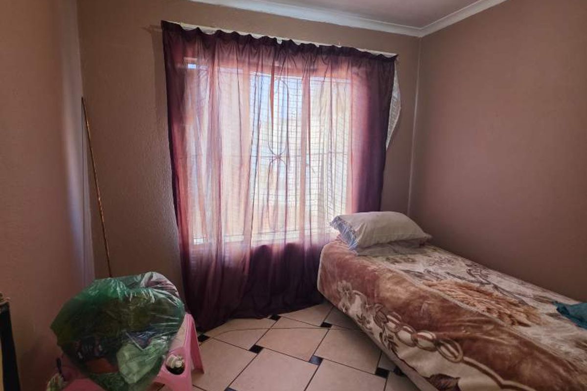 A compact bedroom featuring tiled flooring and a window with curtain fixtures, providing a functional space for rest.