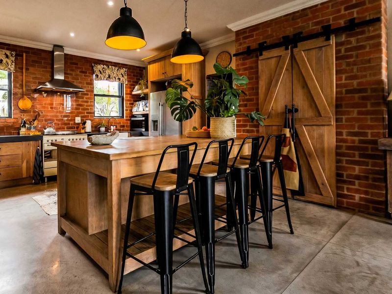 A stylish industrial-themed kitchen featuring exposed brick walls, a large wooden island, concrete floors, and a functional sliding barn door.