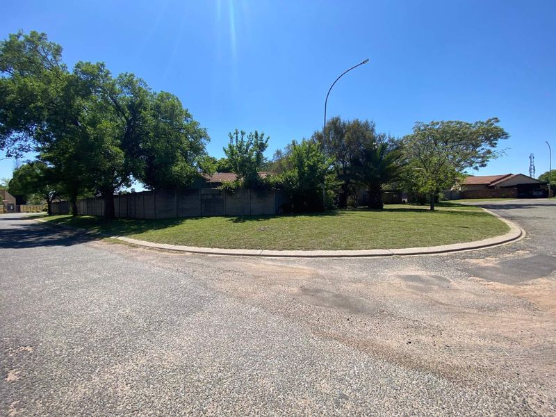 A street-level view of the property corner, featuring a landscaped verge, mature trees, and a concrete boundary wall.
