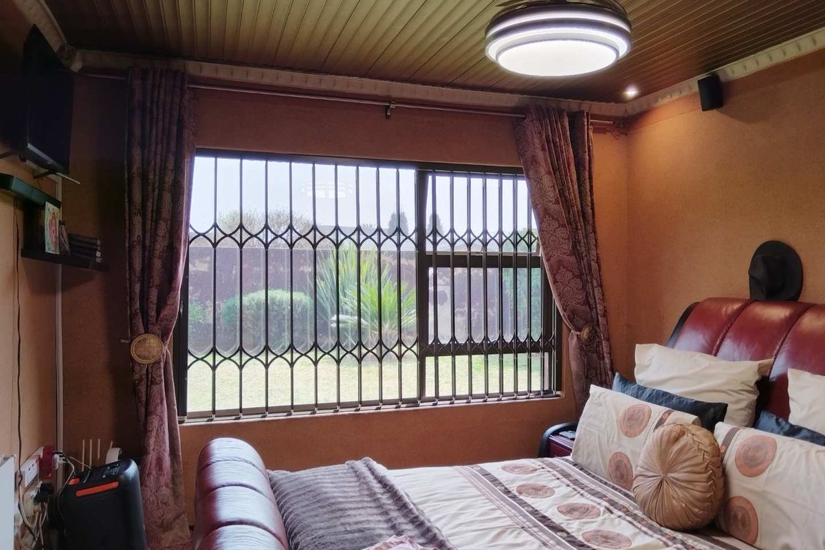 A bedroom featuring a timber ceiling, textured walls, and a window fitted with a security gate.
