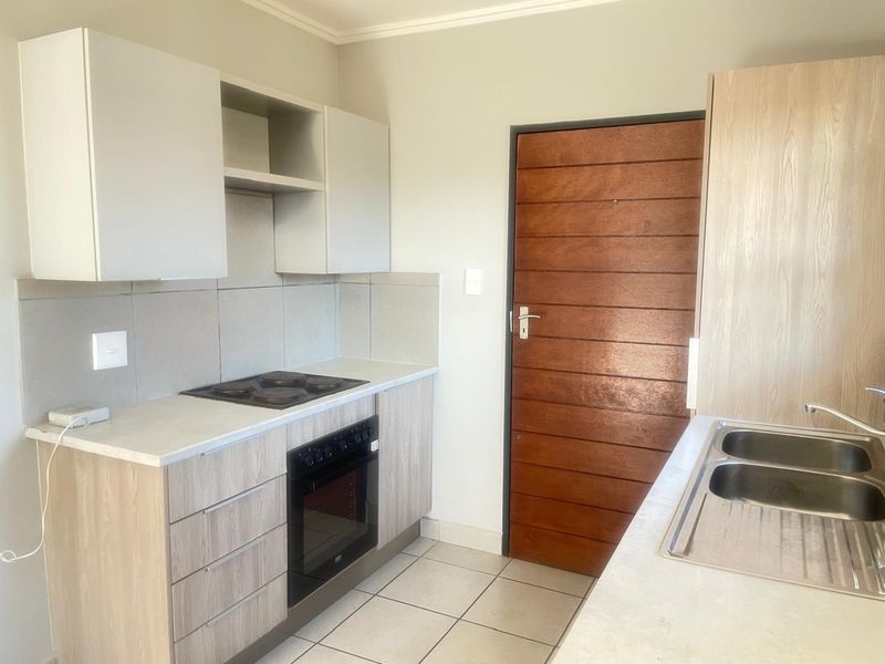 A clean and functional kitchen featuring light wood-look cabinetry, a built-in oven and hob, tiled splashbacks, and a double stainless steel sink.