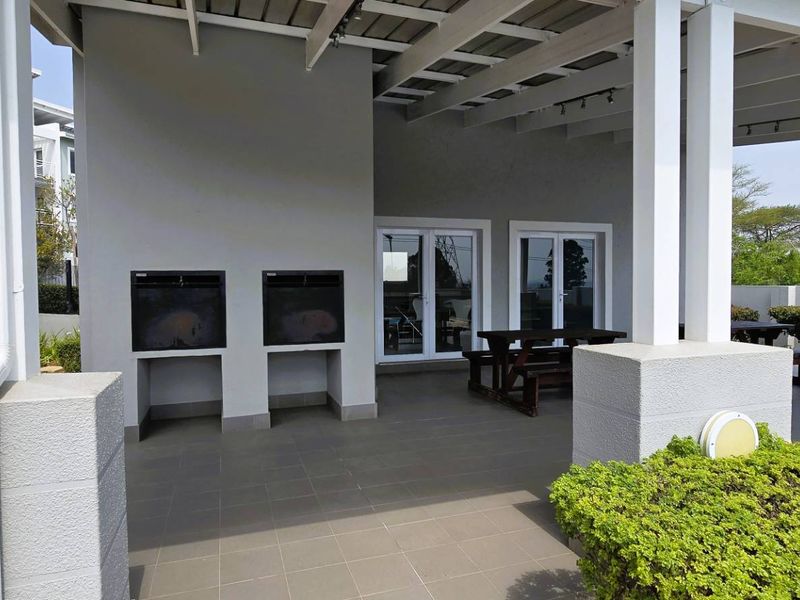 Covered outdoor patio area featuring built-in braai facilities, tiled flooring, and a pergola structure, ideal for outdoor entertaining.