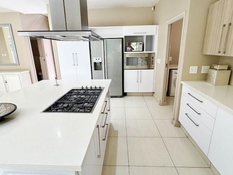 Modern kitchen featuring a central island with a gas hob, extractor fan, built-in appliances, stone countertops, and ample white cabinetry.