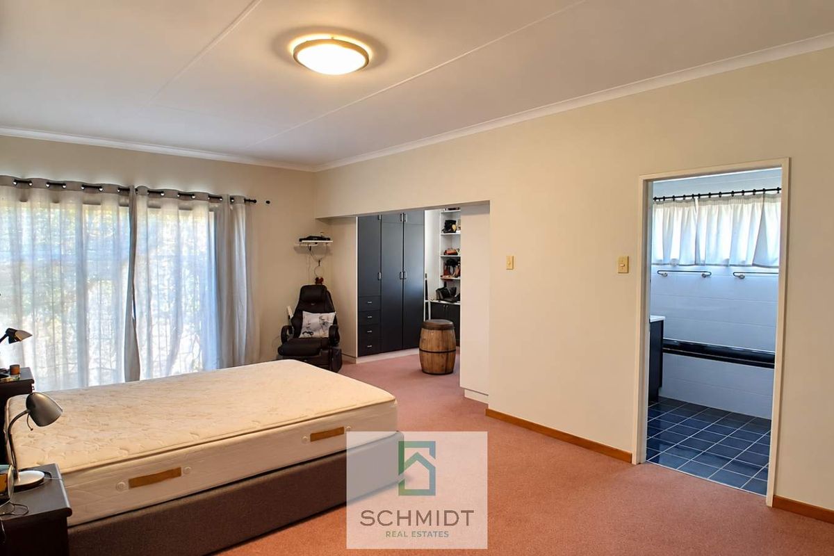 Spacious bedroom featuring built-in cupboards, an en-suite bathroom, and an integrated air conditioning unit.