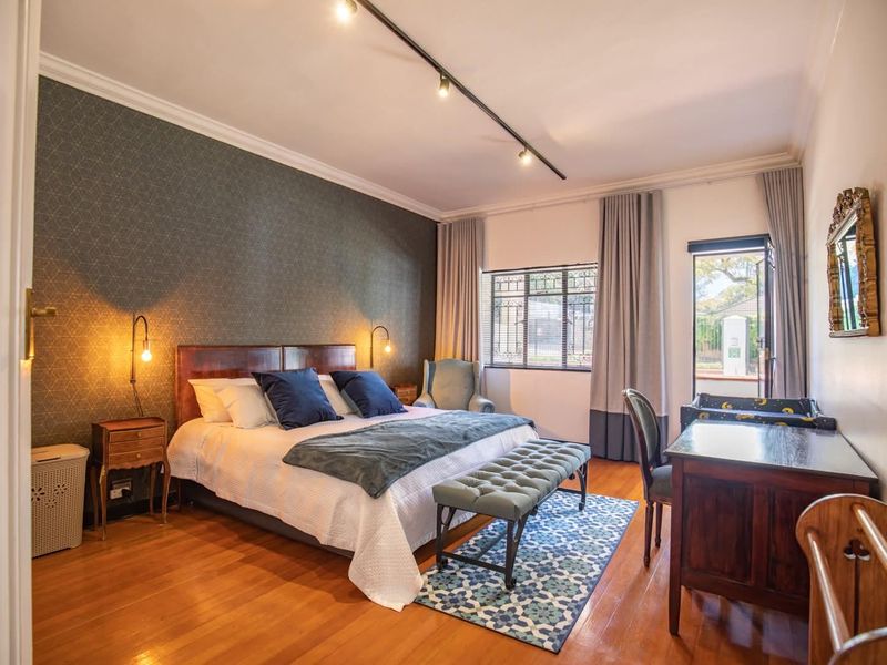 A well-maintained bedroom featuring hardwood flooring, decorative wallpaper, crown molding, and track lighting, with direct access to an outdoor area.