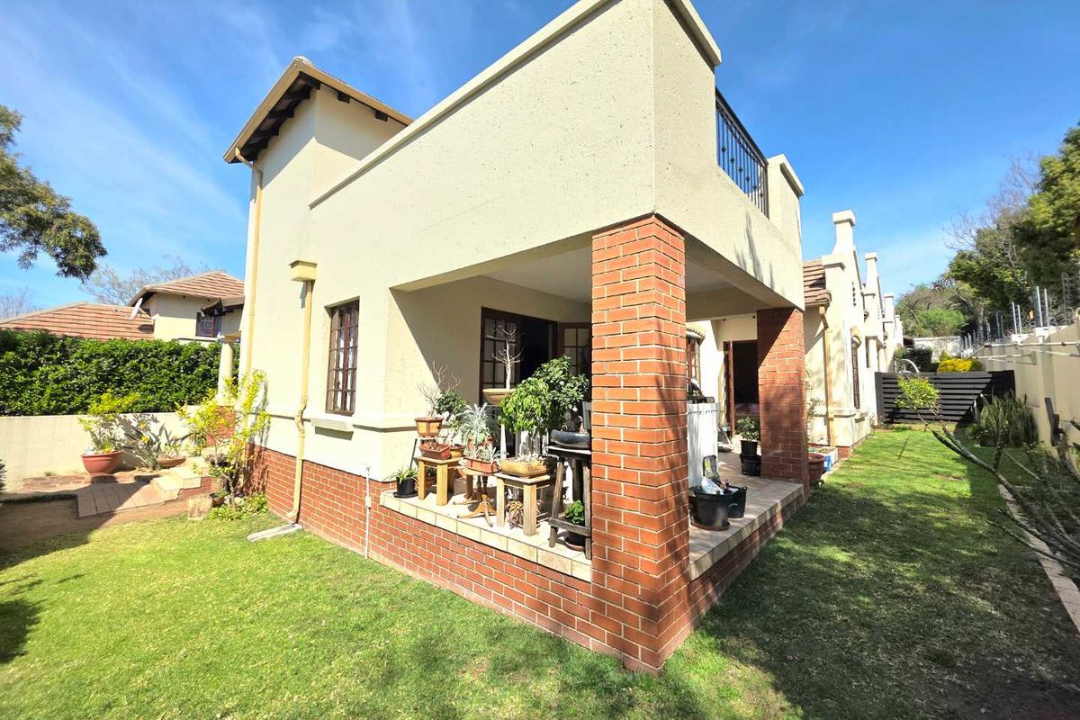 Rear view of the house featuring a covered patio with brick pillars, a balcony with wrought iron railings, and a well-maintained garden area.