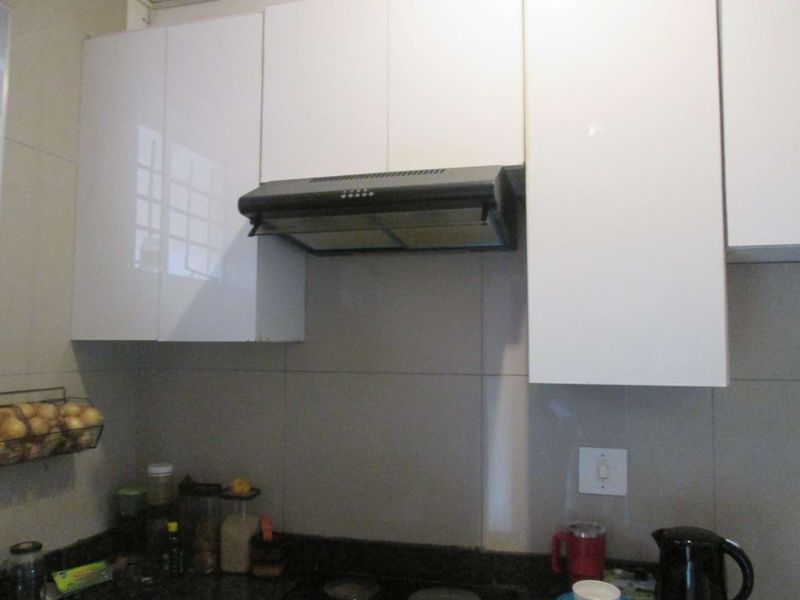 A functional kitchen area featuring white gloss cabinetry, a built-in extractor fan, and a tiled backsplash with a stone countertop.