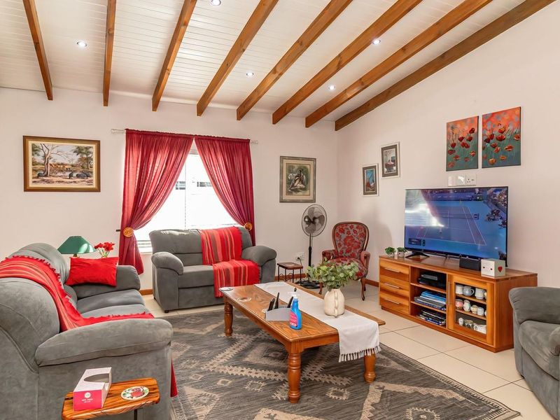 A comfortable living room featuring exposed timber ceiling beams, recessed downlighting, and neutral tiled flooring.