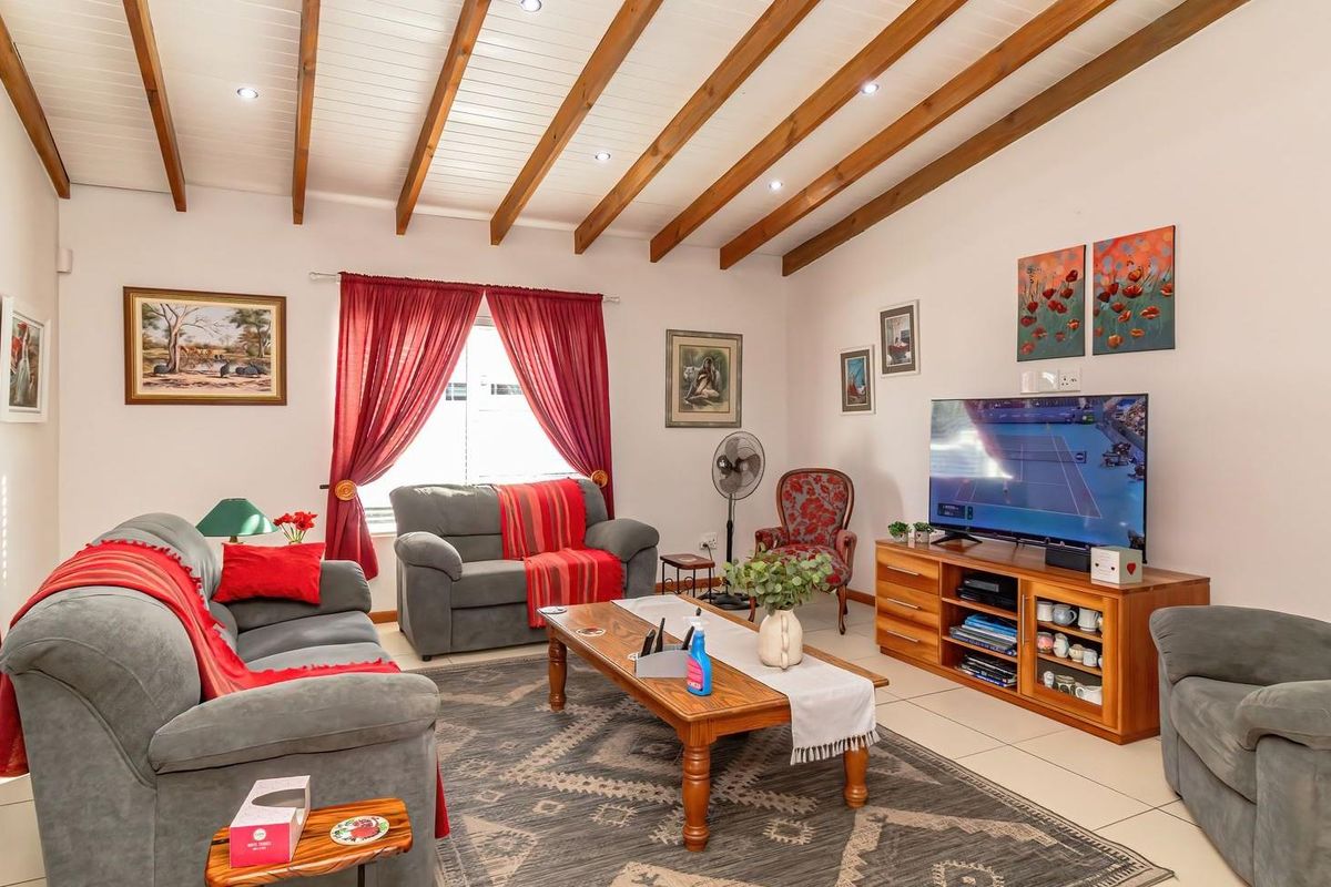 A comfortable living room featuring exposed timber ceiling beams, recessed downlighting, and neutral tiled flooring.